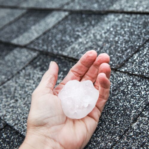 hand holding hail stone next to roof